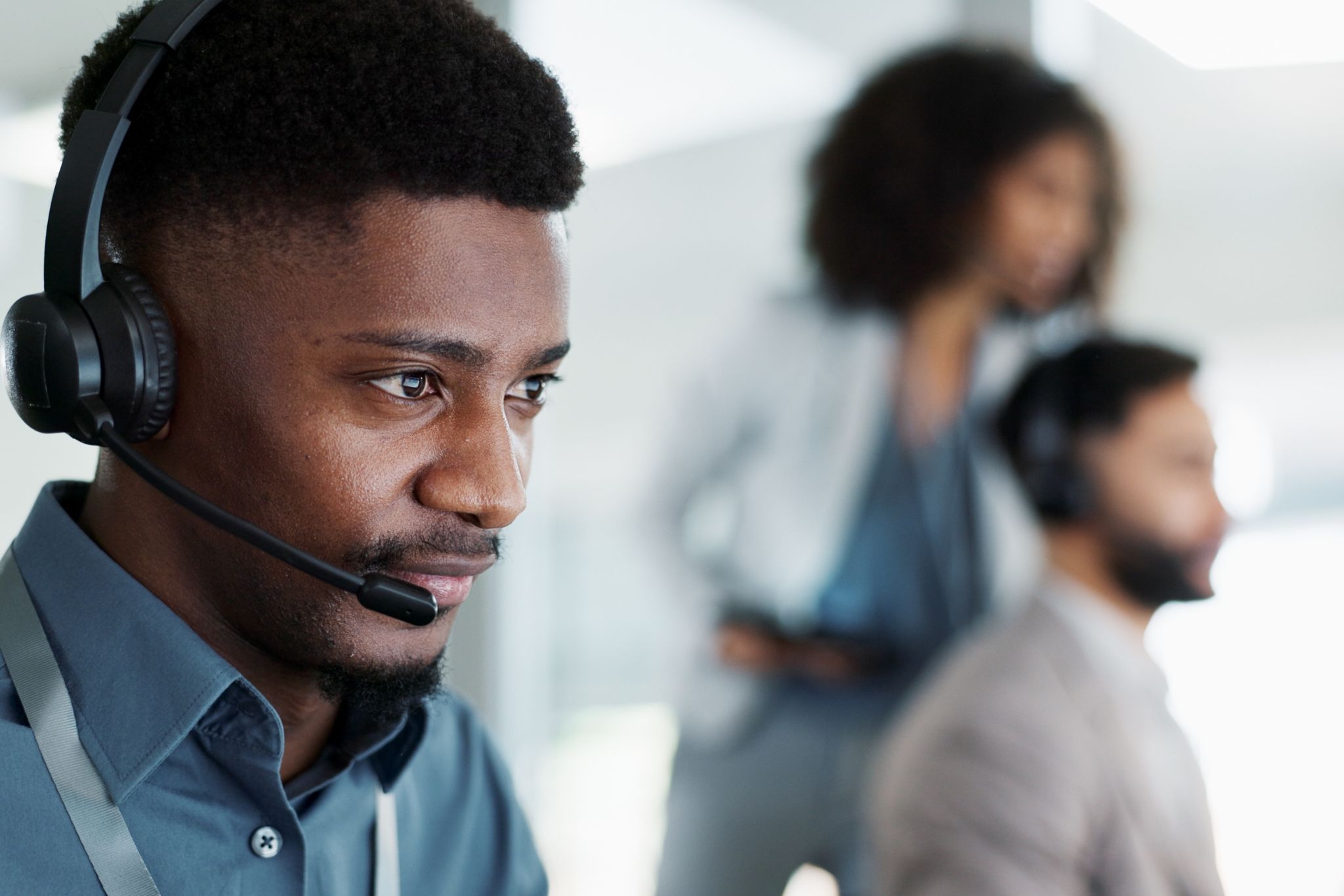 Young African American employee with a headset, concentrating on a laptop in a busy open office environment.