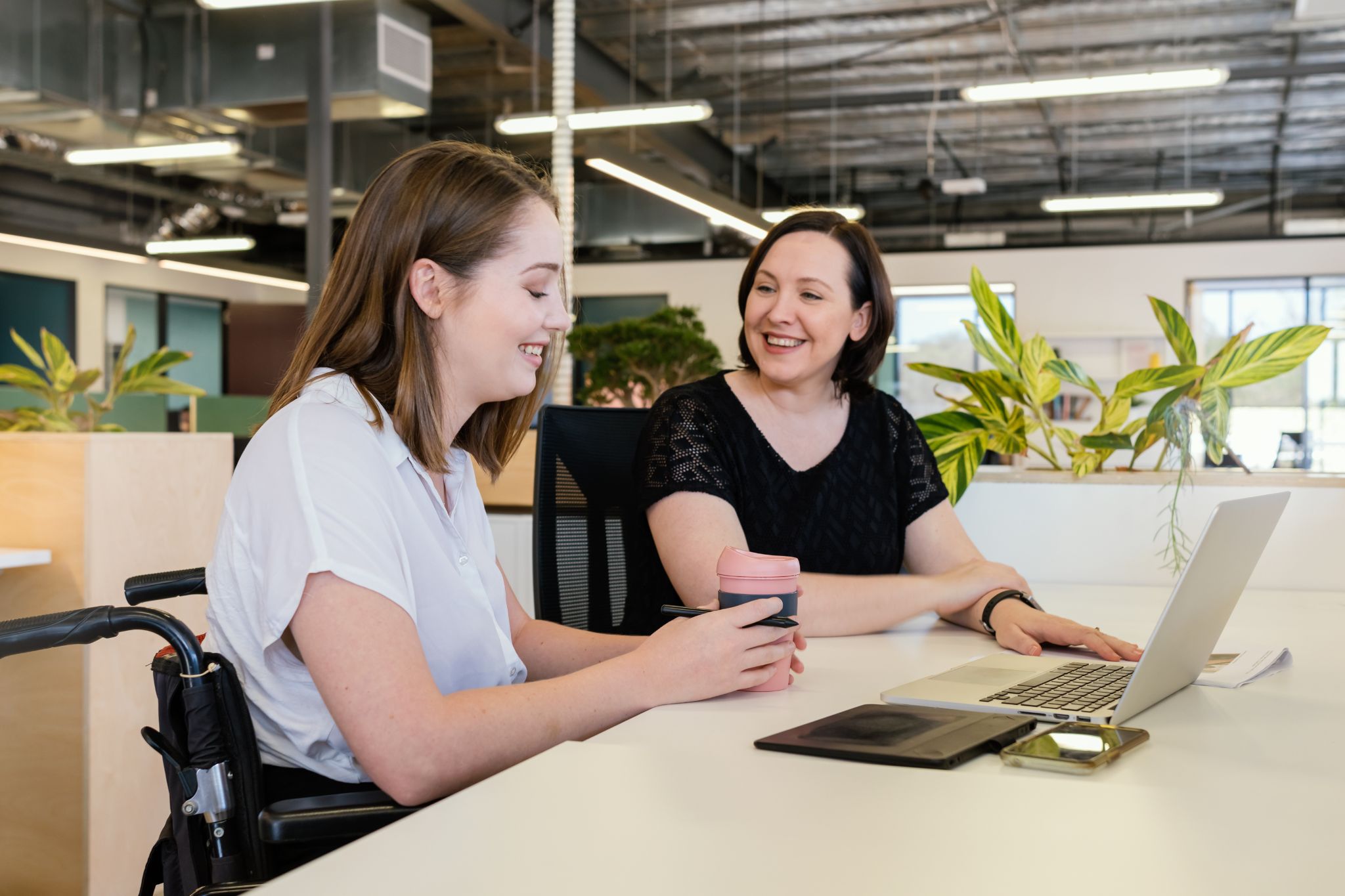 Two female employees sitting in an open office, working on a laptop.